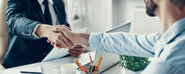Deux personnes se serrent la main dans un bureau, avec des documents sur la table.